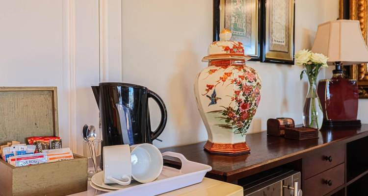 Koffie- en theestation in een gastenkamer met waterkoker, kopjes en decoratieve porseleinen pot.