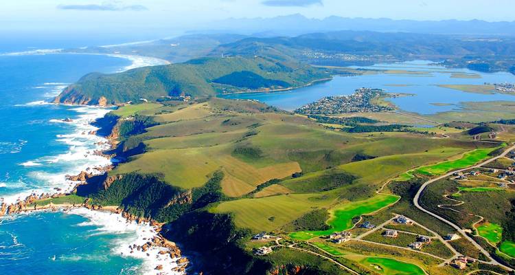 Luchtfoto van de dramatische kustlijn van Knysna, lagune en glooiende groene heuvels die de oceaan ontmoeten.