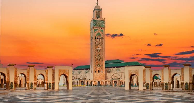 Hassan II-moskee met zijn imposante minaret domineert een open plein onder een schitterende oranje zonsonderganghemel in Casablanca.
