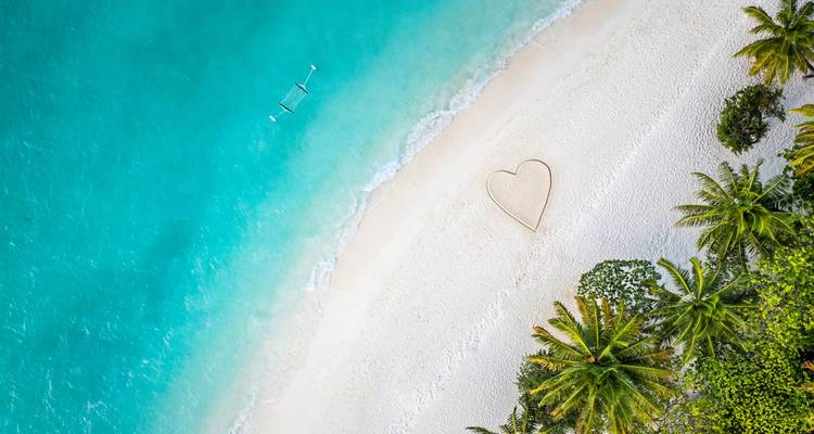 Vue de drone d'une plage immaculée avec un contour en forme de cœur dans le sable et des vagues turquoise