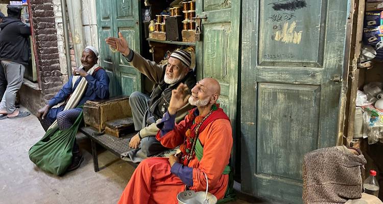 Hombres mayores conversando animadamente fuera de una fachada de tienda de madera verde desgastada en un callejón de bazar tradicional.