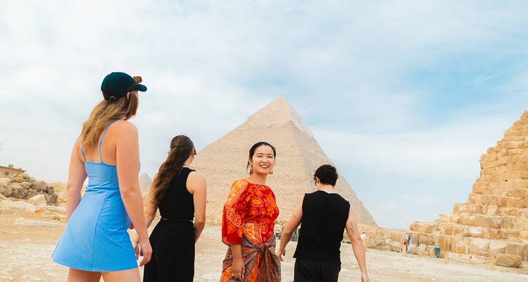 Group of young travelers smiling and walking near the Great Pyramid with bright desert sky overhead.