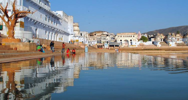 Pilgrims and visitors on ghats around holy Pushkar Lake with whitewashed buildings reflected in water