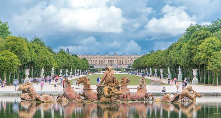 Fuente de Latona con visitantes desenfocados y gran avenida arbolada hacia el Palacio de Versalles
