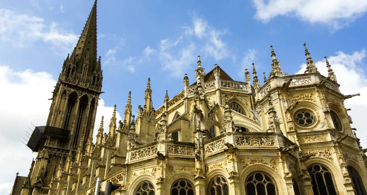 Cathédrale gothique de Rouen avec des sculptures de pierre ornées et une haute flèche contre un ciel bleu.