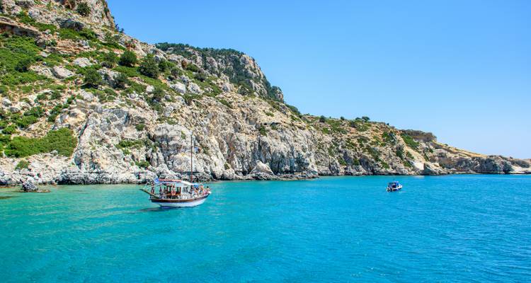 Bateau traditionnel en bois ancré dans une baie turquoise éclatante adossée à des falaises calcaires escarpées.