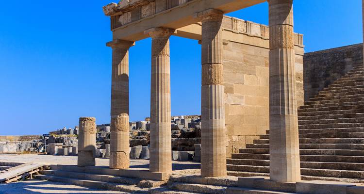 Colonnes de pierre et marches de l'ancienne Acropole de Lindos sous un ciel bleu dégagé.