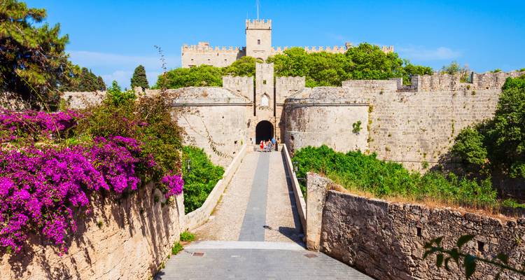Approche bordée de fleurs vers les murs de pierre médiévaux et la porte de la vieille ville de Rhodes.