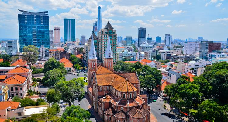 Vue aérienne de la cathédrale Notre-Dame d'Hô Chi Minh-Ville parmi les gratte-ciel modernes et les boulevards bordés d'arbres.