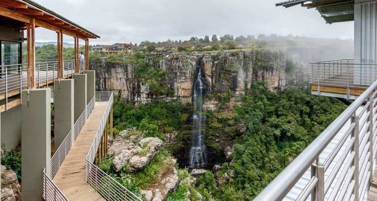 Mirador moderno con vista a una cascada alta que se precipita hacia un cañón verde y exuberante.