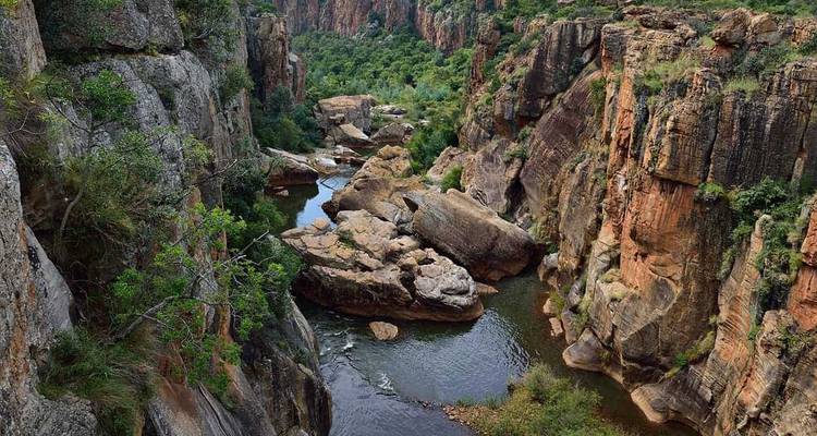 Desfiladero rocoso con arroyo corriente y empinadas paredes de arenisca cubiertas de vegetación.