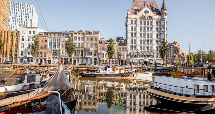Historisch Witte Huis en oude havenboten weerspiegeld in stil water te midden van eclectische Rotterdamse architectuur.