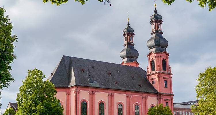 Pink baroque church with twin onion-domed towers framed by leafy trees