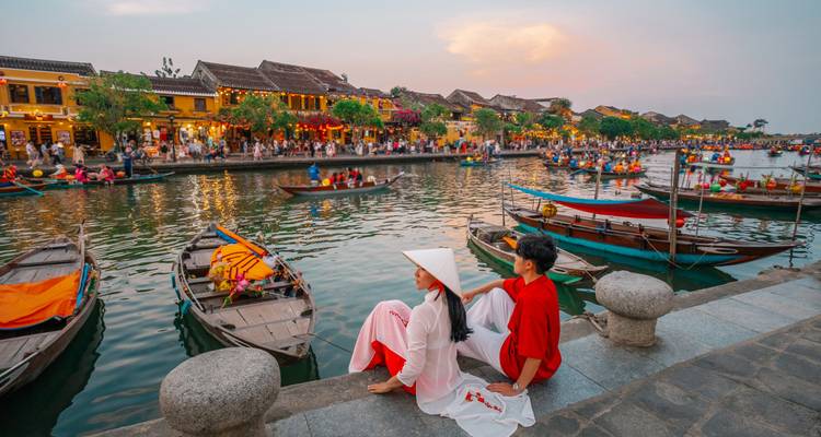 Couple en tenue traditionnelle contemplant les bateaux éclairés par des lanternes sur la rivière de Hoi An au crépuscule.