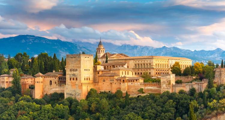 Vue panoramique de la forteresse et du palais de l'Alhambra au coucher du soleil avec un ciel coloré et des montagnes au-delà