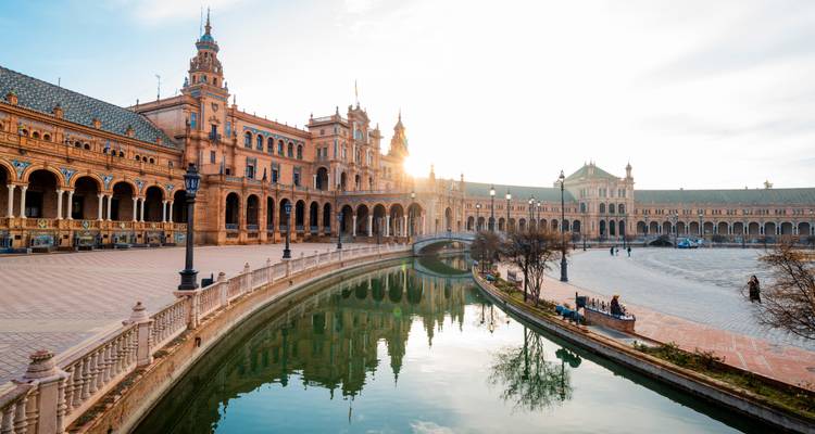 Soleil matinal brillant à travers les arches de la Plaza de España se reflétant dans un canal sinueux