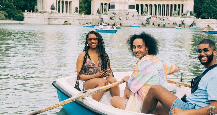 Des amis ramant dans une petite barque sur le lac tranquille du parc du Retiro avec le palais en arrière-plan.