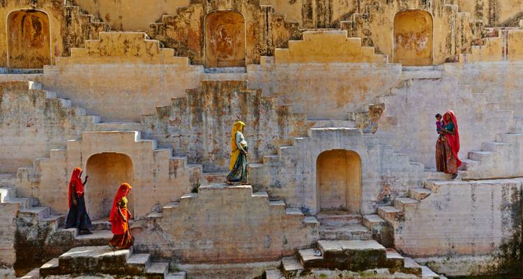 Frauen in farbenprächtiger traditioneller Kleidung steigen die symmetrischen Treppen eines alten Stufenbrunnens in Rajasthan hinab.