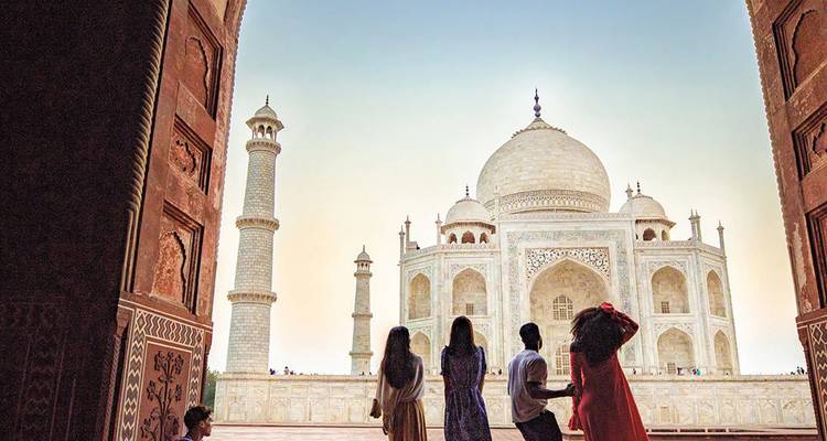 Los visitantes enmarcados por un gran arco admiran el Taj Mahal de mármol blanco al amanecer.