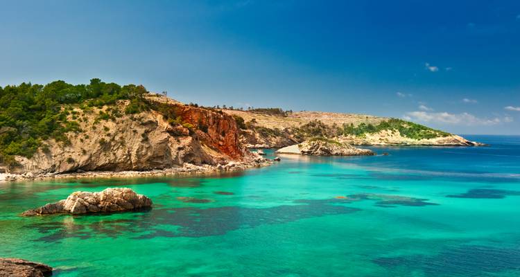 Scenic coastal headland with red and white rocky cliffs plunging into vibrant turquoise sea.