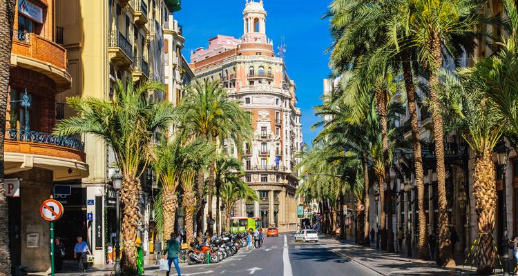 Lebhafte, palmengesäumte Straße in Valencia mit verzierten Gebäuden, Geschäften und Fußgängern.