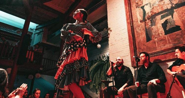Flamencotänzerin in lebendigem Kleid, die auf einer kleinen Innenbühne zusammen mit Live-Musikern auftritt.