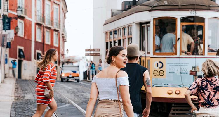 Le tramway de Lisbonne traverse des rues colorées tandis que les voyageurs marchent le long des voies pavées dans le quartier d'Alfama.