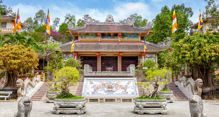 Ornate Vietnamese pagoda entrance flanked by dragon statues and colourful flags.
