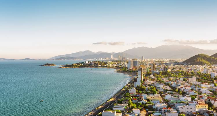 Aerial coastal view of Nha Trang city with long beachfront and mountain backdrop.