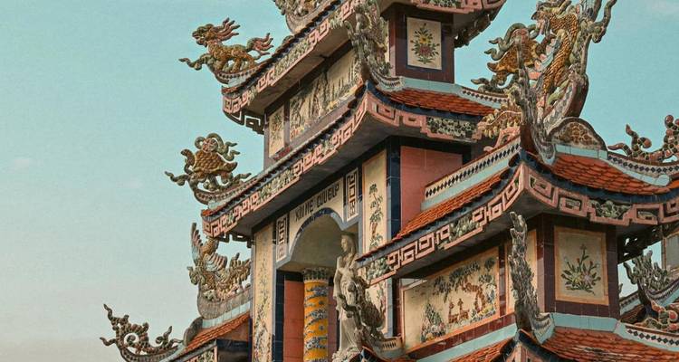 Tour de temple vietnamienne ornementée à plusieurs étages décorée de dragons colorés et de motifs de carrelage complexes sous un ciel dégagé