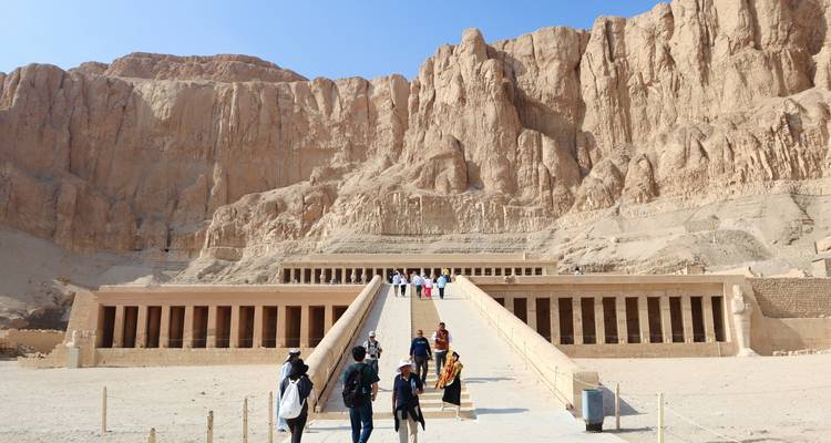 Visitantes ascendiendo la gran rampa hacia el templo mortuorio excavado en roca de Hatshepsut respaldado por acantilados