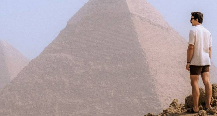 Viajero parado en terreno rocoso mirando la Gran Pirámide de Giza envuelta en la bruma del desierto.