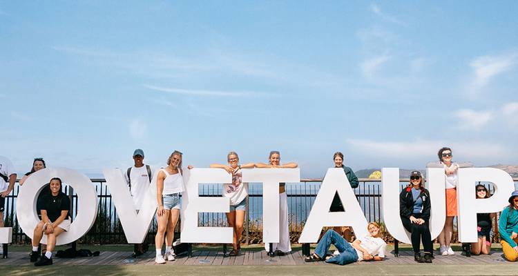 Eine große Gruppe posiert um riesige weiße Buchstaben, die LOVE TAUPO buchstabieren, auf einer Uferpromenade am See.