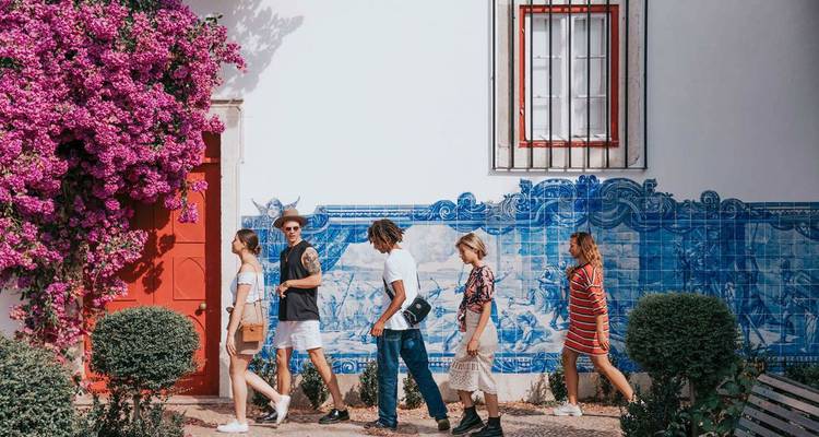 Un grupo pasea junto a azulejos azules y blancos y buganvillas vibrantes en una calle portuguesa.
