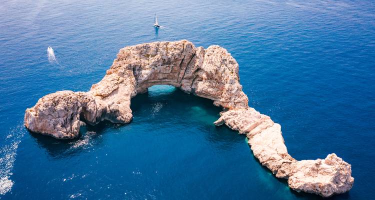 Toma aérea de un arco de piedra natural que se eleva desde las profundas aguas azules del Mediterráneo.