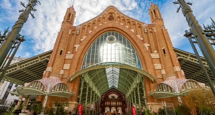 Gran entrada arqueada del Mercado de Colón en Valencia con intrincado trabajo de ladrillo y techo de cristal.
