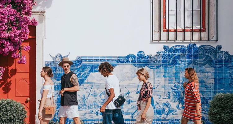Ligne de jeunes voyageurs marchant devant un mur d'azulejos bleus aux carreaux vibrants avec des bougainvilliers roses.