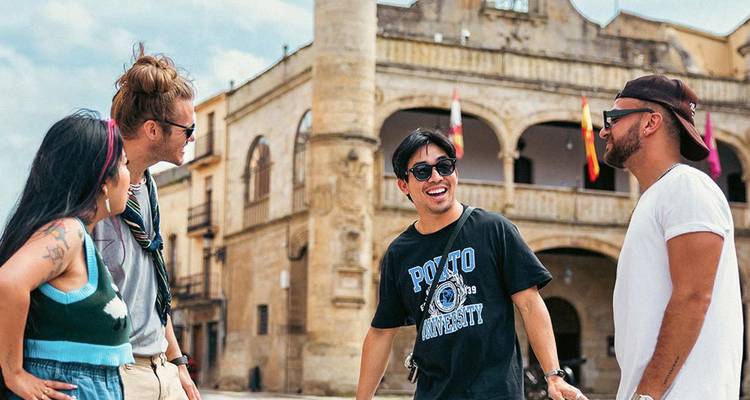Freunde, die zusammen lachen auf einem historischen spanischen Platz mit Steinarkaden und Flaggen.