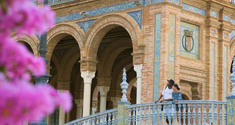 Les visiteurs admirent le pont en céramique détaillé de la Plaza de España encadré par des fleurs roses.