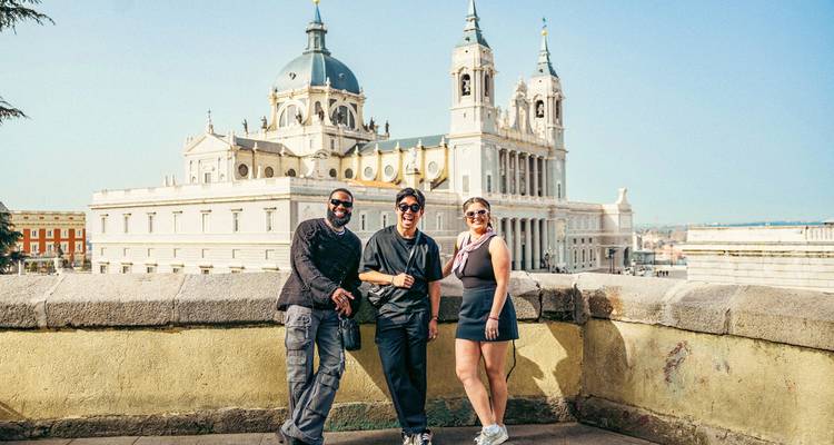 Los viajeros posan ante la gran Catedral de la Almudena de Madrid bajo un cielo azul despejado.