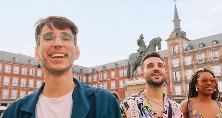 Drei junge Erwachsene lächeln auf der Plaza Mayor mit historischen roten Gebäuden und Reiterstatue