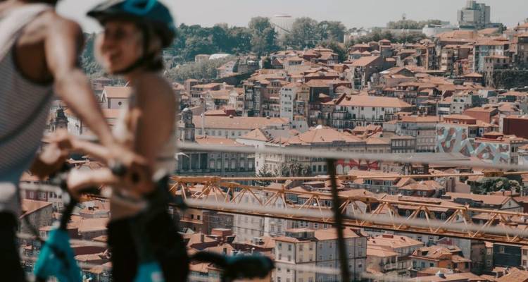 Des cyclistes surplombant les toits en terre cuite et les collines de Porto par une journée ensoleillée.