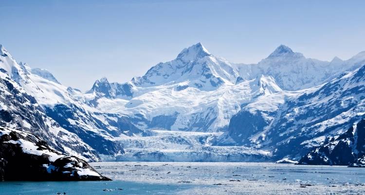 Towering icy mountains and vast tidewater glacier descending to a chilly fjord dotted with ice.