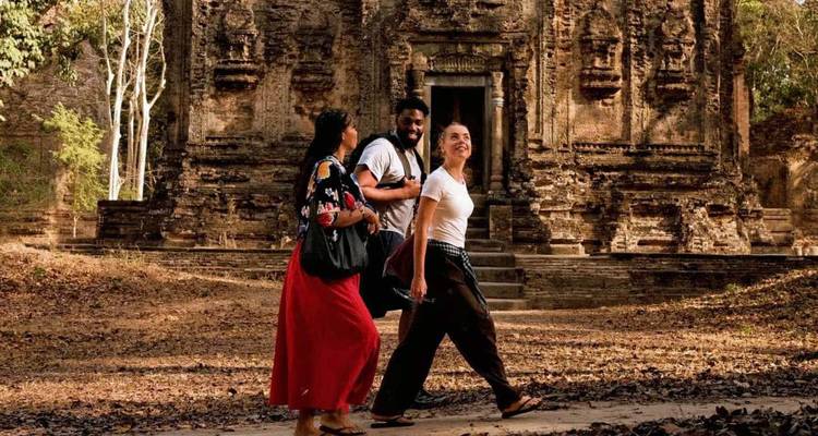 Drie reizigers die langs een oud Angkor-tempel lopen die versierd is met ingewikkelde steensnijwerk