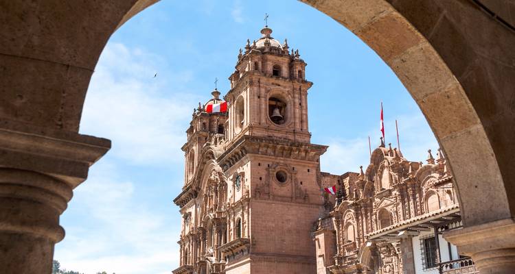 Stone colonial cathedral bell tower framed by a stone arch against bright blue sky in Cusco