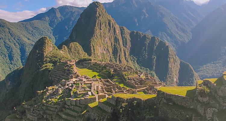 Ruinas de Machu Picchu vistas desde arriba con exuberantes picos circundantes bañados en cálida luz solar.