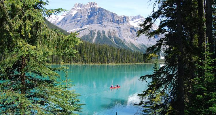 Canoë rouge avec pagayeurs glisse sur le lac Emerald bleu cristallin encadré par des conifères et des sommets