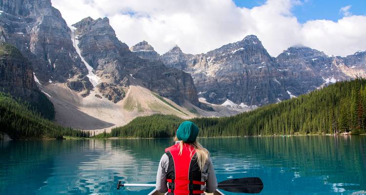 Personne pagayant en canoë sur un lac bleu cristallin entouré de sommets imposants des montagnes Rocheuses et de pins denses.