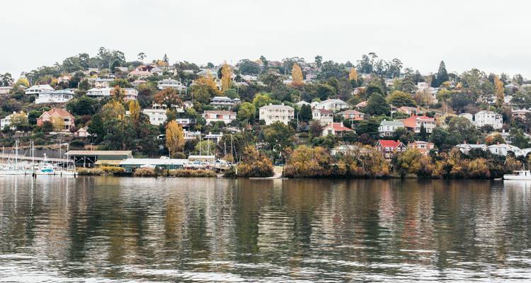 Quiet waterfront scene of Launceston’s leafy hillside suburbs reflected in the Tamar River on an overcast day.
