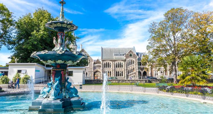 Fontaine victorienne et Centre des Arts de Christchurch encadrés par un ciel bleu et des jardins.